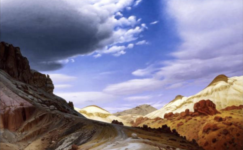 A winding dirt road curves through a rocky, semi-arid landscape with tan hills and red boulders under a dramatic sky filled with large, dark clouds and patches of bright blue.