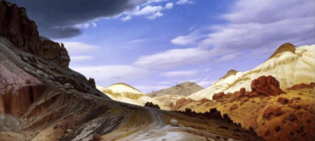 A winding dirt road curves through a rocky, semi-arid landscape with tan hills and red boulders under a dramatic sky filled with large, dark clouds and patches of bright blue.