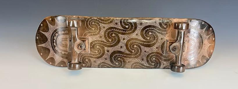 A skateboard with ceramic wheels and deck, featuring intricate, swirling patterns and designs engraved on the surface, displayed against a neutral gray background.