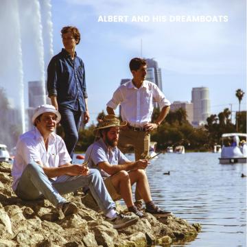 Four men are sitting and standing on rocky ground by a lake under a clear sky. Three are sitting, while one stands, all dressed casually. A cityscape with tall buildings and a jet of water from a fountain are visible in the background. Text reads "ALBERT AND HIS DREAMBOATS.