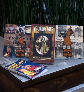 A wooden bench holds a display of cowboy-themed cookbooks and a poetry book titled "Cowboy Love Poetry." Books feature rustic imagery, recipes, and Western motifs. Decorative metal art shaped like boots and a hat is also present.