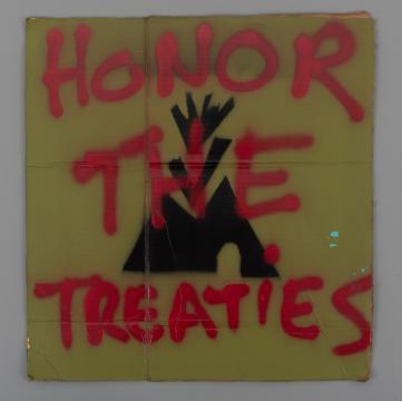 A cardboard sign with red spray-painted text reading "HONOR THE TREATIES" over a stenciled black teepee symbol on a yellow background.