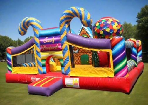 A colorful inflatable bounce house with candy-striped pillars, a large ball covered in multicolored spots, and a sign that reads "Candy Playground," set on green grass under a clear blue sky.
