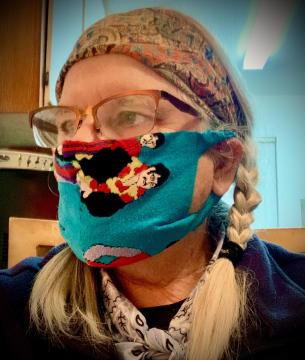 woman with braided hair wearing glasses, and a blue mask with red, white and black design