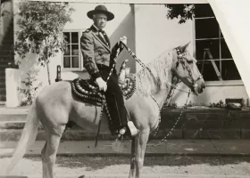 black and white photograph of a man riding a horse, with the reins in his left hand