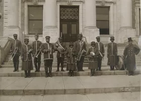 black and white photograph of an all-Black musical band on the steps of a courthouse, carrying various instruments