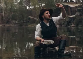 prospector inspects nugget in body of water