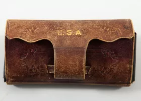 Vintage, well-worn brown leather pouch with intricate embossed designs and the letters "U.S.A" stamped in gold at the top. The pouch appears to have a flap closure and shows signs of aging with a slightly faded texture.