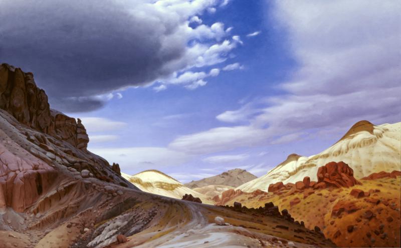 A dramatic desert landscape with rocky hills, reddish and tan earth, winding paths, and a sky filled with large, swirling clouds under bright blue.