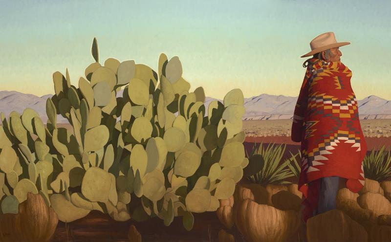 A person wearing a wide-brimmed hat and a colorful patterned blanket stands next to a large cactus in a desert landscape with mountains in the distance under a clear sky.