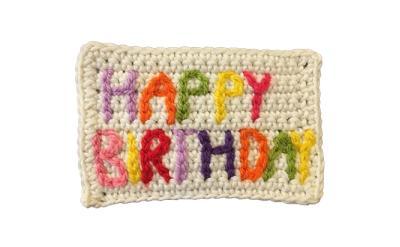 crochet rectangle made with white yarn, with the words "happy birthday" spelled out in colorful crochet letters