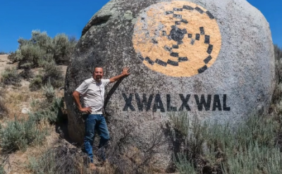 An artist leans on his intervention in nature, a large rock painted