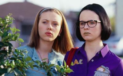 two girls staring in distance partially hidden by a shrub