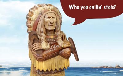A wooden cigar store Indian wearing a headdress and holding his flip flops with the ocean behind him. A speech bubble is shown with the words “Who you callin’ stoic?”