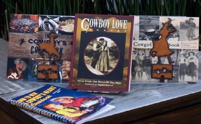 A collection of Western-themed books and cookbooks displayed on a table, featuring titles like "Cowboy Love Poetry," "The Cowboy's Cookbook," and "The All-American Cowboy Cookbook." Decorative cowboy-shaped ornaments are also present.