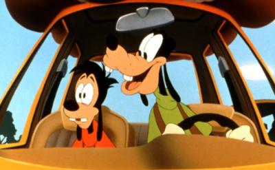 Animated characters, a tall dog in a green shirt and a smaller dog in a red shirt, are in a car. The tall one is driving and smiling, while the smaller one looks anxious. The view is from the front, showcasing a bright, cartoonish environment.