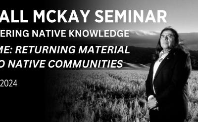 Black-and-white image of a long-haired person in a suit standing in a field with hills in the background. Text reads: "Marshall McKay Seminar for Empowering Native Knowledge: Going Home: Returning Material Culture to Native Communities. Nov 15-16, 2024.
