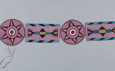 A beaded belt with alternating circular and rectangular motifs in pink, blue, yellow, black, and white, featuring geometric patterns and some loose thread ends.