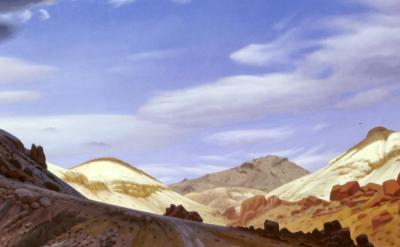 A wide desert landscape with rocky hills, golden sand dunes, scattered red boulders, and a partly cloudy blue sky.