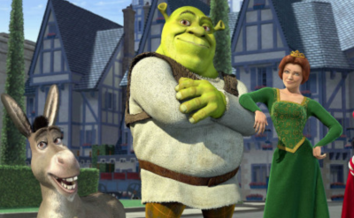 Animated characters Donkey, Shrek, Fiona, and Lord Farquaad stand posing confidently in front of medieval-style buildings and a castle wall in daylight.