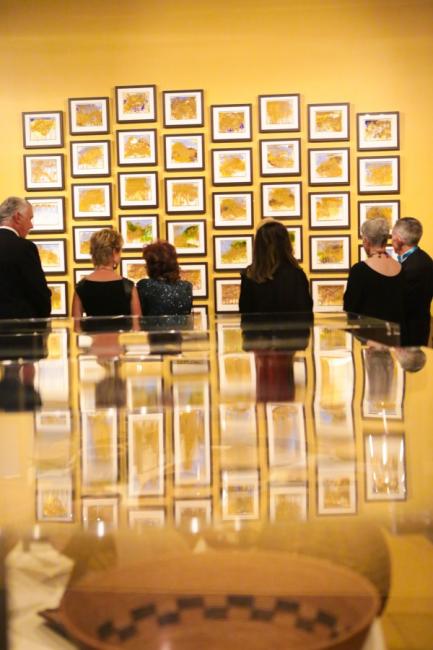 people stare at a gallery with many framed yellow watercolors
