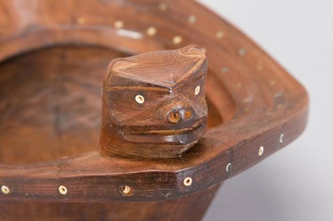 a detail of a wooden bowl with carved bear heads as handles
