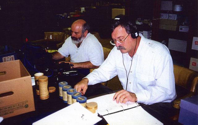 two men working at a table wearing headphones working with wax cylinders