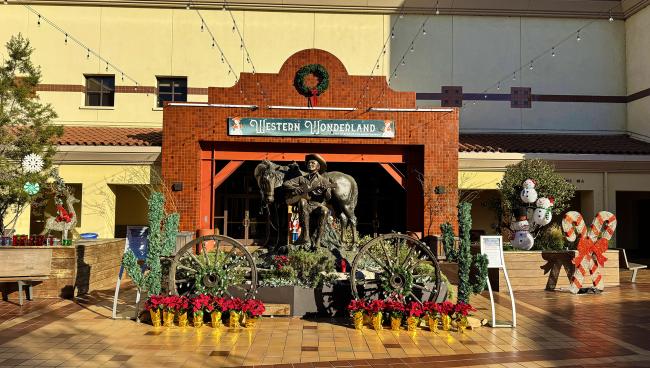 A festive "Western Wonderland" display features a cowboy scene with a horse statue, surrounded by wagon wheels, poinsettias, and decorations, including snowmen and candy canes, set in a sunny mall courtyard.