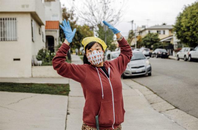 A woman with patterned mask and surgical gloves raises her hands in the air