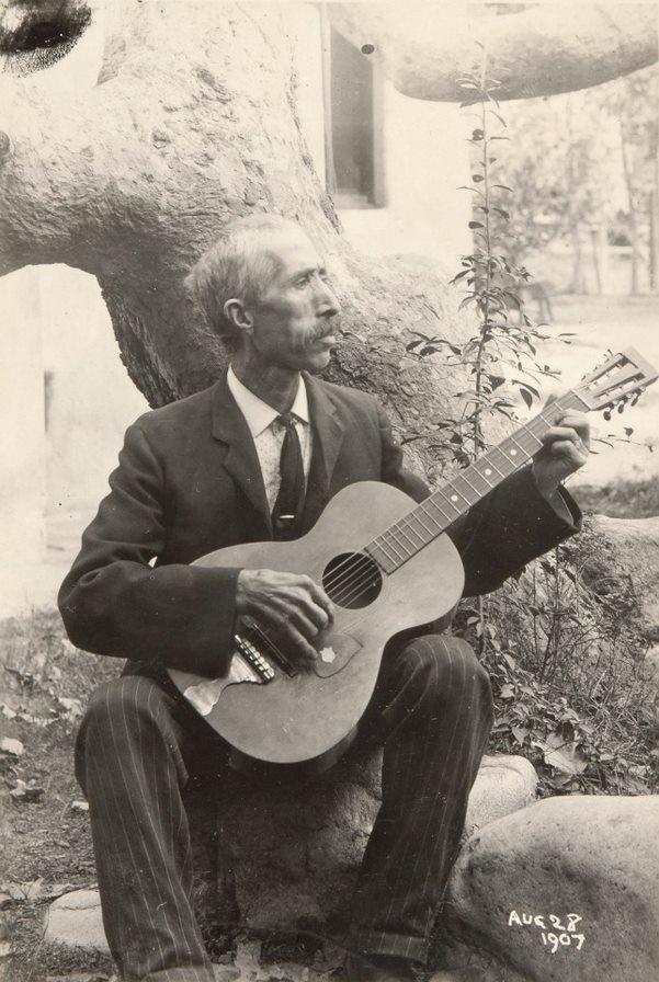 man sitting at base of tree playing guitar