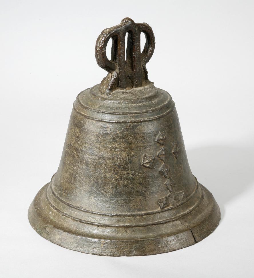 A weathered, metal bell with a simple handle and a row of small, raised diamond-shaped decorations on its side, photographed against a plain white background.