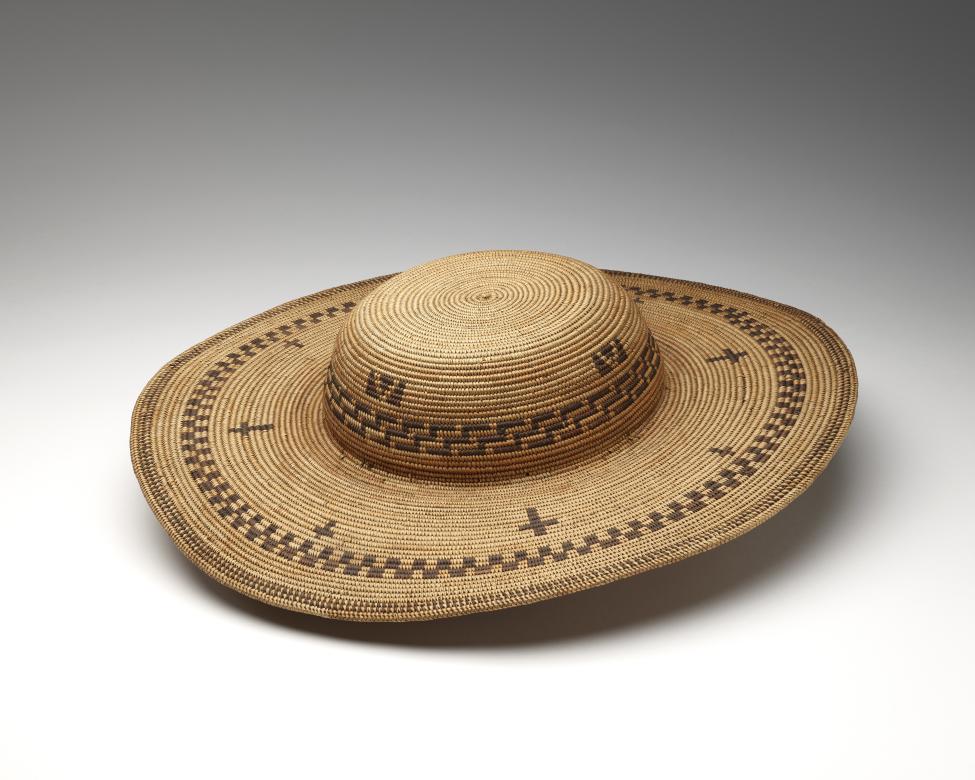 A wide-brimmed, woven hat with a rounded crown, featuring geometric patterns in dark and light natural fibers arranged in bands and crosses around the brim and crown.