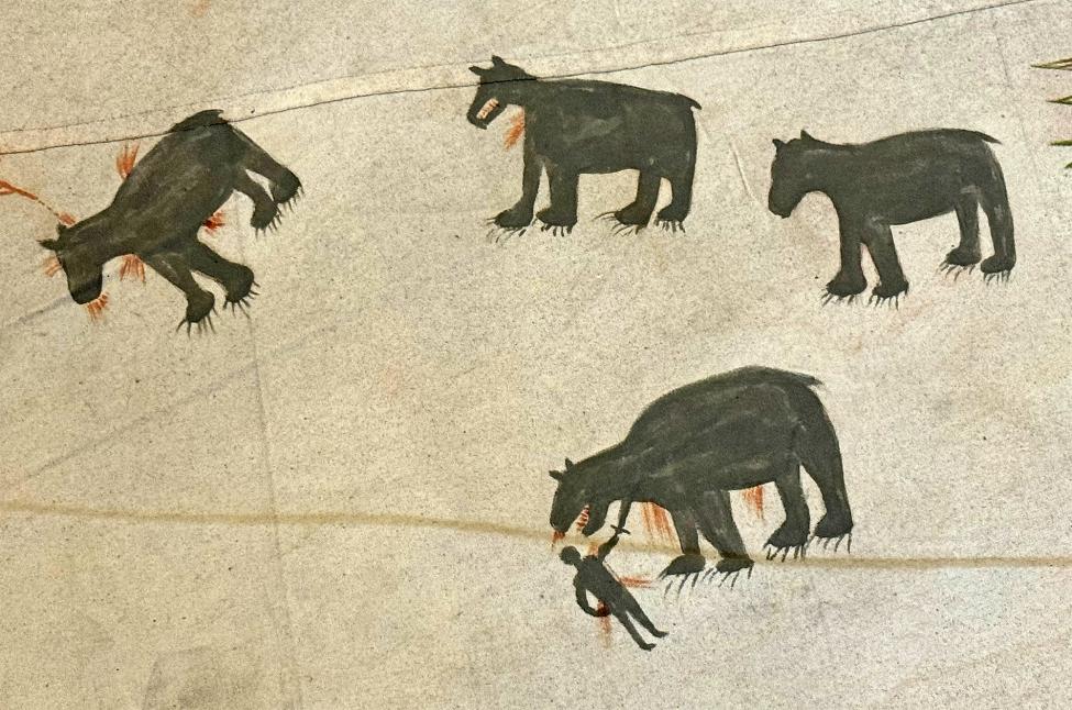 A drawing shows four black bear-like animals with red markings, one of which is biting a human figure. The animals and human appear on a beige background, likely part of an ancient or indigenous artwork.
