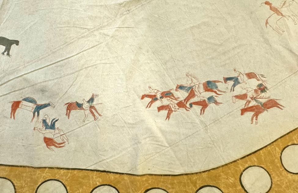 A painted scene on a tan surface shows figures on horseback, some holding weapons, in red, blue, and brown. Horses and riders appear in motion near a yellow, circular border at the bottom.