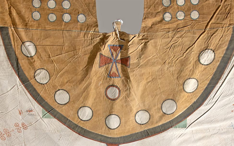 A tan Native American hide shirt featuring a semicircular yoke decorated with white circles, a red and blue cross design in the center, and faint red and green designs on the lower edges.