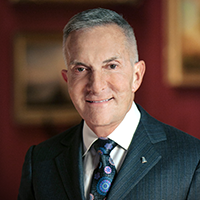 Portrait of a man wearing a dark suit, white collared shirt, and a dark patterned tie.