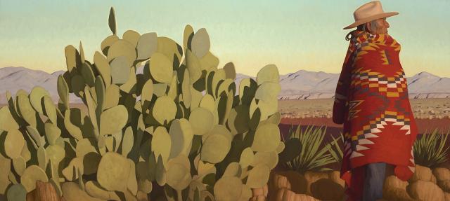 A person wearing a wide-brimmed hat and a colorful patterned blanket stands next to a large cactus in a desert landscape with mountains in the distance under a clear sky.