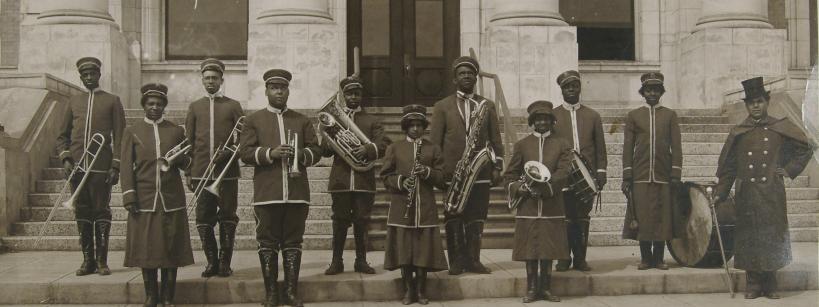 black and white photograph of an all-Black musical band on the steps of a courthouse, carrying various instruments