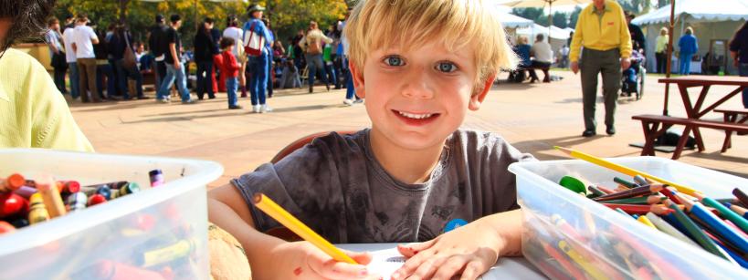 Boy looks at camera and smiles while drawing