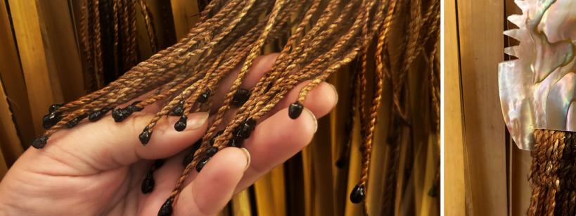 A hand holding a bunch of brown, twisted cords with black tips. On the right, a shiny, decorative object with a wavy, iridescent design is attached to similar cords. The background features more cords hanging vertically.