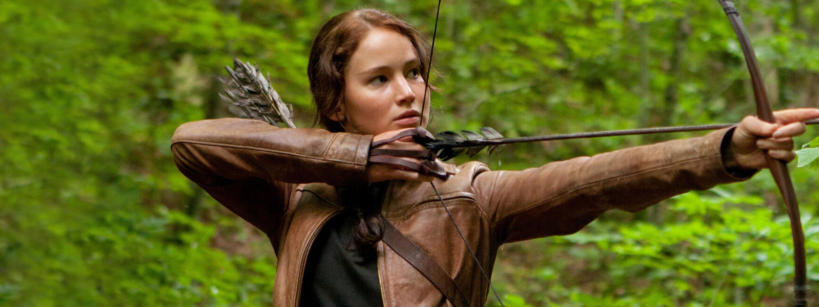 A young woman with brown hair, wearing a brown jacket and quiver, draws a bow and aims an arrow in a lush green forest.