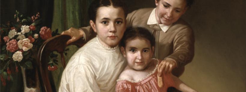 Three children pose indoors with a brown dog. Two girls sit in front—one in a white dress on a chair, the other in a pink dress petting the dog. A boy stands behind them, smiling as he feeds the dog. A vase of flowers sits nearby.