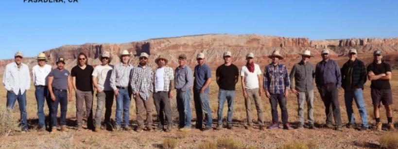 A group of about 20 people stands side by side outdoors with rocky cliffs in the background. Text above announces an artist retreat group exhibition in Pasadena, CA on October 17 & 18, 2025, and mentions a VIP weekend event.