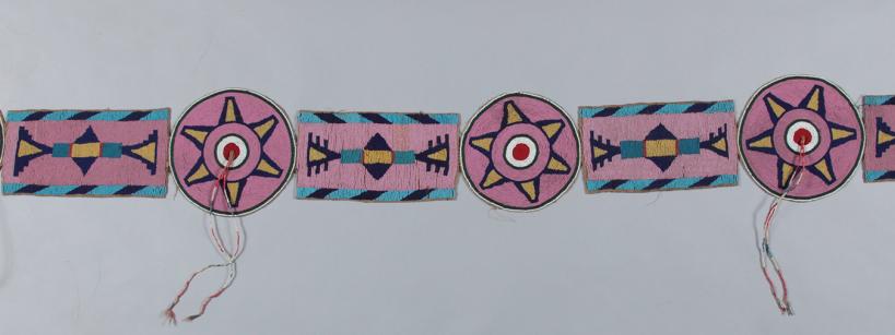 A beaded belt with alternating circular and rectangular motifs in pink, blue, yellow, black, and white, featuring geometric patterns and some loose thread ends.