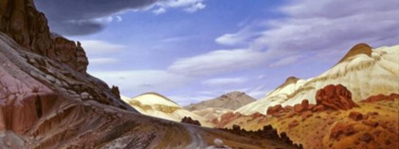 A winding dirt road curves through a rocky desert landscape with reddish and tan hills under a partly cloudy blue sky.