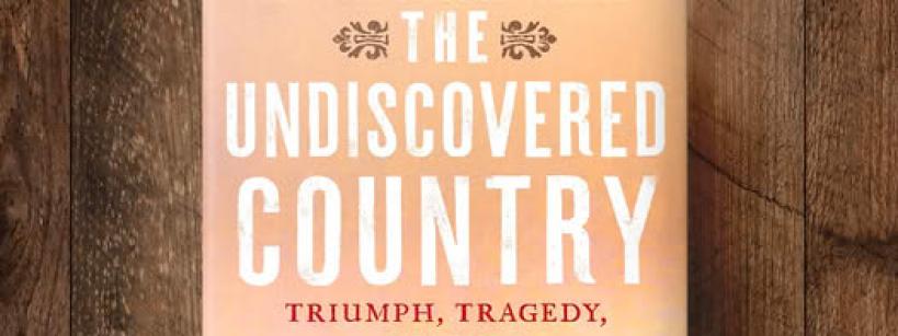 Book titled "The Undiscovered Country" by Paul Andrew Hutton on a wooden surface. The cover shows a group of people on horseback in a western landscape at sunset.