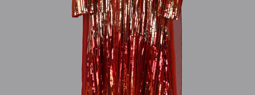 A long, red, pleated gown covered in shiny sequins, with long sleeves and a high neckline, displayed against a plain gray background.